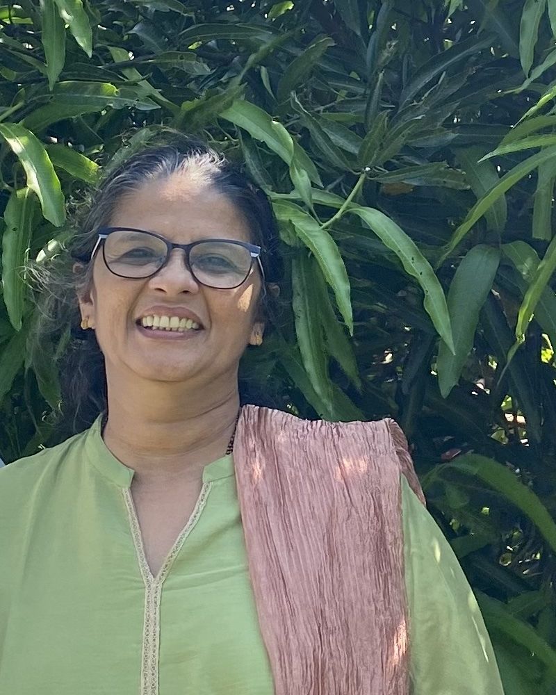 Sheela Mariyam Oommen smiling in a garden, wearing a green kurta and rose dupatta.